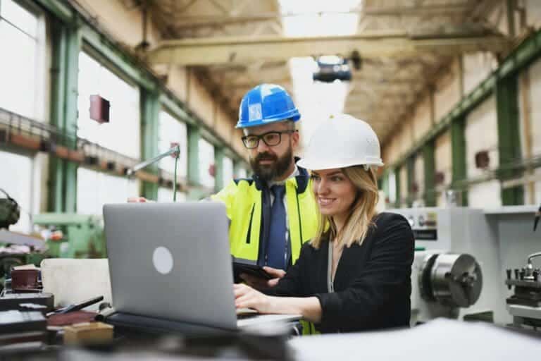 Male and female industrial engineers discussing factory's new machinery project and using laptop.